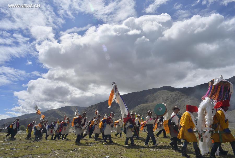 Farmers in holiday array carry scriptures while attending an Ongkor Festival prayer ceremony in Bomtoi Village, Dagze County, Lhasa, southwest China's Tibet Autonomous Region, July 1, 2014. By walking around farmlands, villagers of the Tibetan ethnic group pray for good harvests during the annual Ongkor Festival, or Bumper Harvest Festival. [Photo/Xinhua]