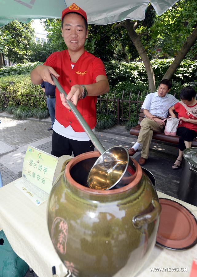 A volunteer adds Longjing green tea to the tea barrel, near the West Lake, Hangzhou, capital of east China's Zhejiang Province, July 9, 2014. Free tea was provided to people at six Volunteer Smile Pavilions along the West Lake in Hangzhou, from 10:00 to 14:00 every day. The service, provided since the summer of 2012, will last for three months starting in July this year. [Photo/Xinhua]