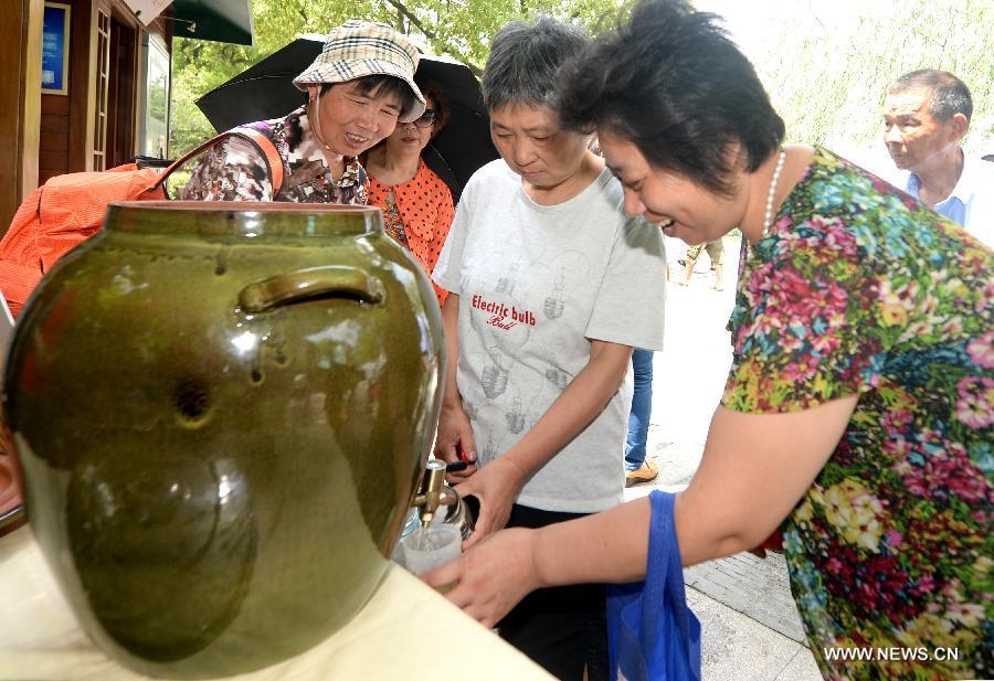 Visitors fill free Longjing green tea in their bottles at a Volunteer Smile Pavilion near the West Lake, Hangzhou, capital of east China's Zhejiang Province, July 9, 2014. Free tea was provided to people at six Volunteer Smile Pavilions along the West Lake in Hangzhou, from 10:00 to 14:00 every day. The service, provided since the summer of 2012, will last for three months starting in July this year. [Photo/Xinhua]