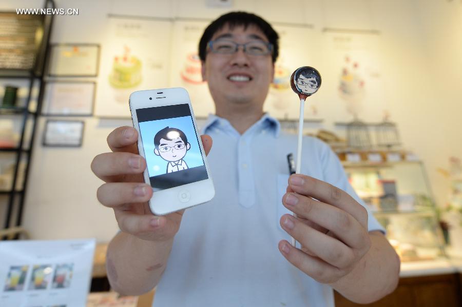 A staff of a local bakery demonstrates a lolipop customized after his own cartoon avatar created by MYOTee, a popular mobile phone-based personal profile picture creator, in Shenyang, capital of northeast China's Liaoning Province, July 9, 2014. [Photo/Xinhua]