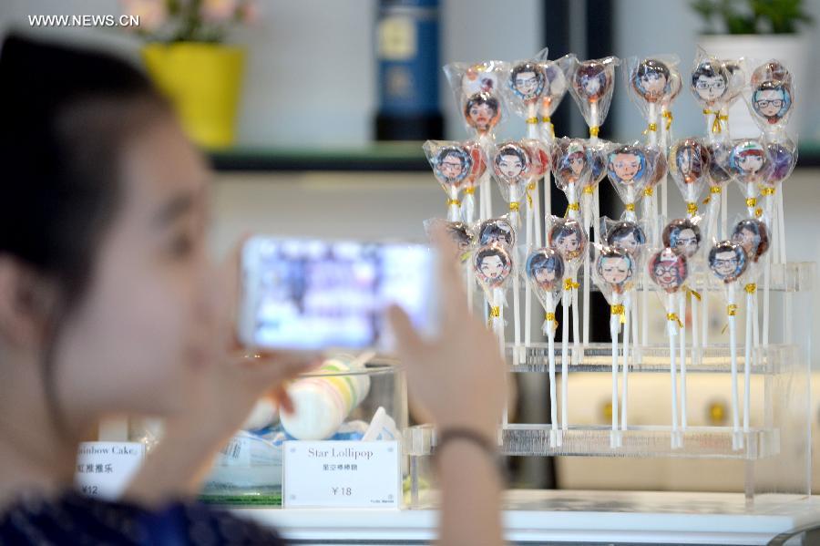 A customer takes photos of lolipops customized after cartoon avatars created by MYOTee, a popular mobile phone-based personal profile picture creator, at a local bakery in Shenyang, capital of northeast China's Liaoning Province, July 9, 2014. [Photo/Xinhua]