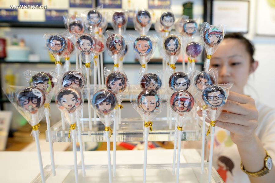 A staff of a local bakery demonstrates lolipops customized after cartoon avatars created by MYOTee, a popular mobile phone-based personal profile picture creator, in Shenyang, capital of northeast China's Liaoning Province, July 9, 2014. [Photo/Xinhua]
