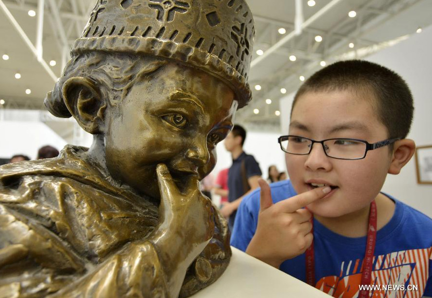 A boy imitates the gesture of a sculpture during the 1st Xinjiang International Art Biennale in Urumqi, capital of northwest China's Xinjiang Uygur Autonomous Region, June 25, 2014. Hundreds of artworks by 132 artists from 18 countries were presented during the biennale. [Photo/Xinhua]