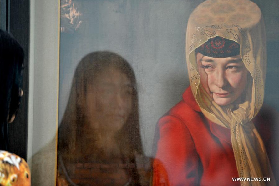 A woman looks at a painting during the 1st Xinjiang International Art Biennale in Urumqi, capital of northwest China's Xinjiang Uygur Autonomous Region, June 25, 2014. Hundreds of artworks by 132 artists from 18 countries were presented during the biennale. [Photo/Xinhua]