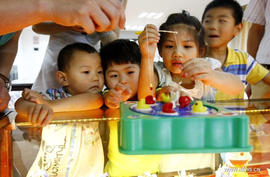 Children play a fishing toy at an old toy exhibition in east China's Shanghai, July 2, 2014. The toys presented on the exhibition, from the collections of 18 collectors, remind visitors born in the 1970s and the 1980s of their childhood. [Photo/Xinhua]
